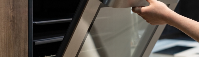 Vertical photo of woman hand opening metallic door on built-in oven in brown wooden kitchen cabinet