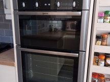 Shiny silver double oven in white kitchen next to spice rack