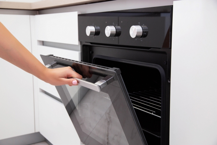 A woman's hand opens the door of an electric convection oven. Built-in oven in the kitchen, energy consumption